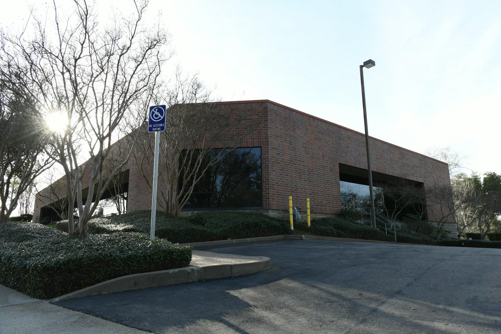 Sunlight illuminates a brick office building with surrounding bare trees.